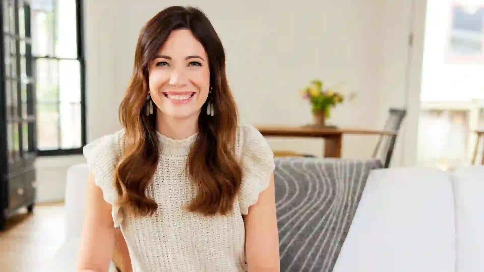 Rachel Cruze smiling at camera while sitting on a couch at a home.