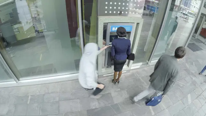Businesswoman being robbed at ATM in broad daylight by male robber.