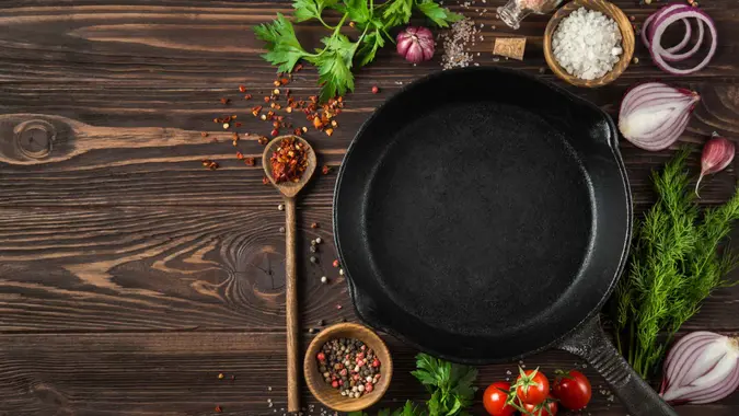 herbs and spices around cast iron skillet on wooden background.