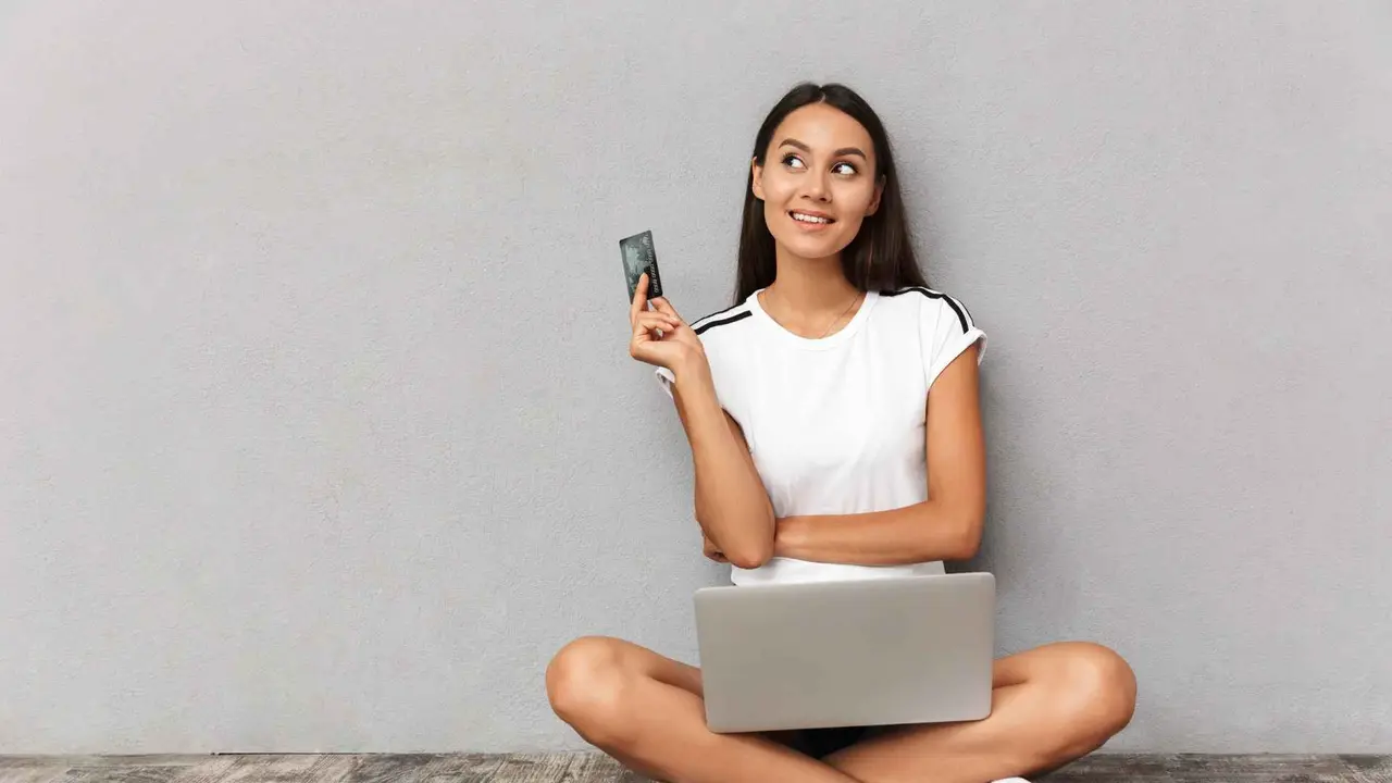Image of beautiful young woman sitting isolated over grey background using laptop computer holding credit card.