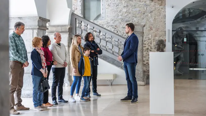 A serious attractive caucasian male museum employee presenting and having a conversation with his group of visitors.