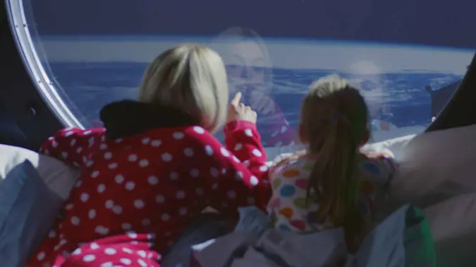 Medium shot of a mother and daughter enjoying view of Earth from spaceship.