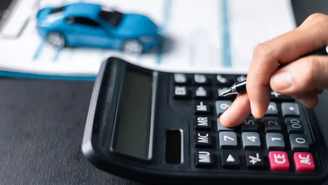 Car dealer calculate interest rate and costs of car loan with calculator, explaining details to customer on term and agreement in dealership office, offering financial and insurance service. stock photo