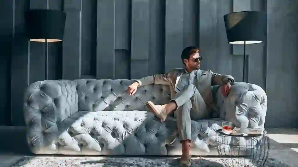Handsome stylish man in beige suit at home sitting on sofa.