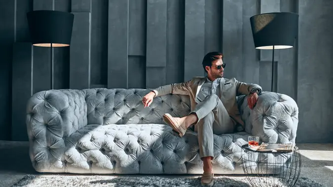 Handsome stylish man in beige suit at home sitting on sofa.