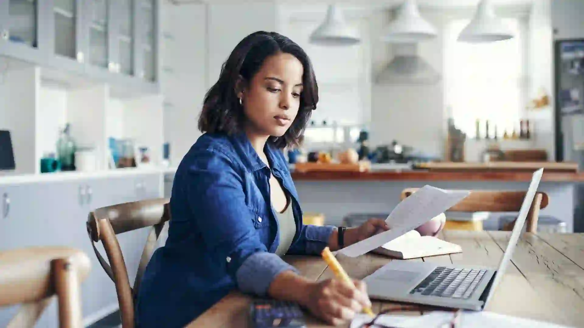 Shot of a young woman using a laptop and going through her paperwork while working from home.