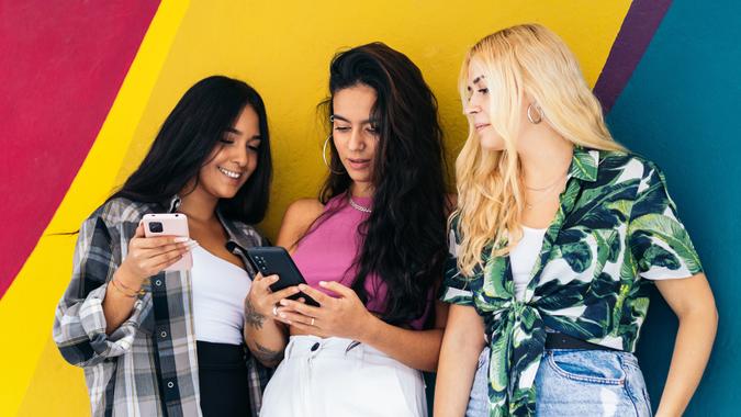 young gen z females on smartphones colorful background_iStock-2042095001 Girls using smartphone outdoors. Colorful background stock photo
