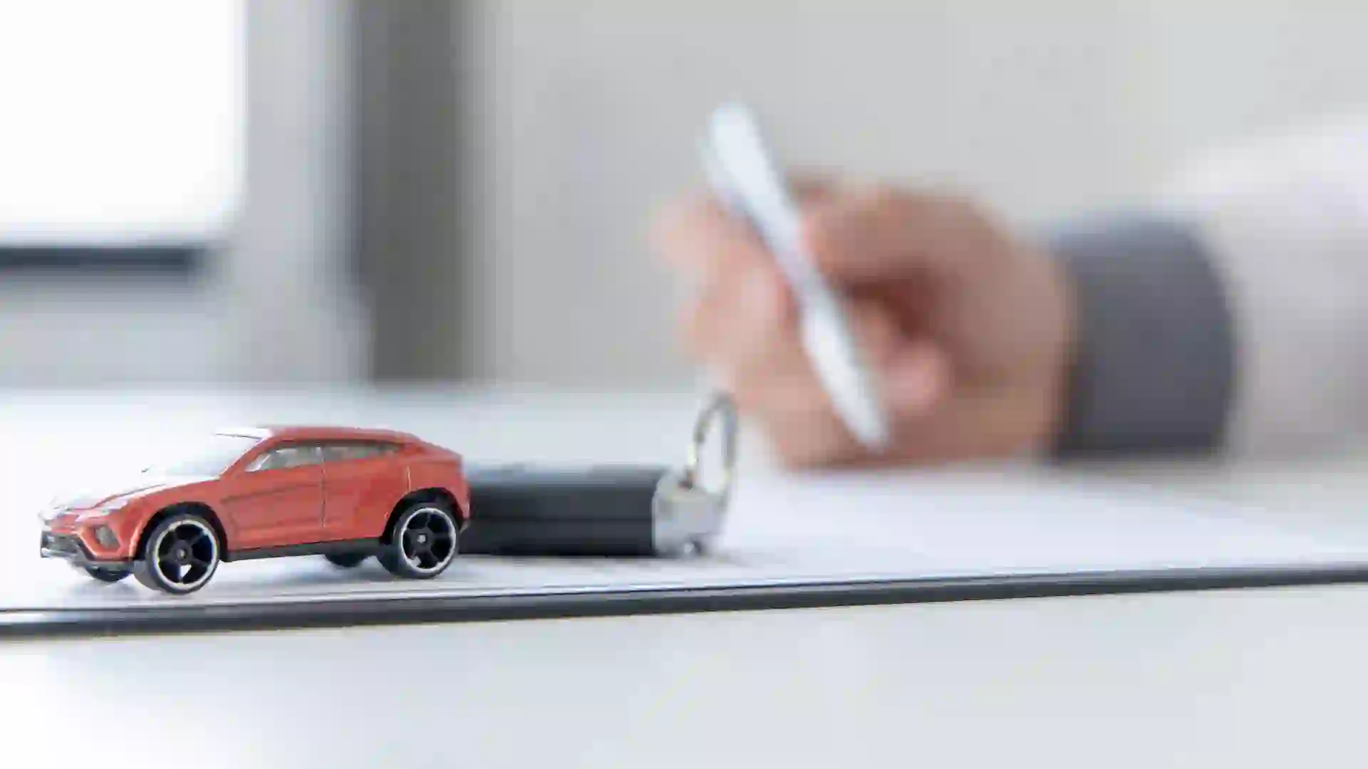 Hand signing papers next to a car toy and keys