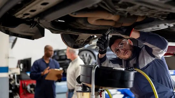 Latin American mechanic working at an auto repair shop fixing a car - vehicle breakdown concepts.