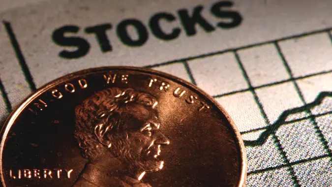 Stacks of coins with miniature figures and a graph represent a penny stocks investing concept.