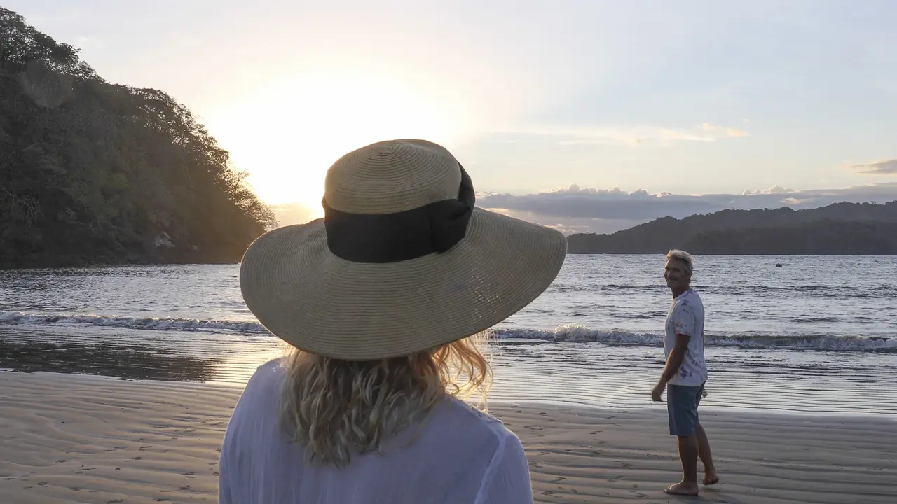 Mature couple walk along beach at sunrise stock photo