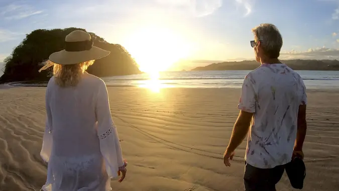 Mature couple walk along beach at sunrise stock photo