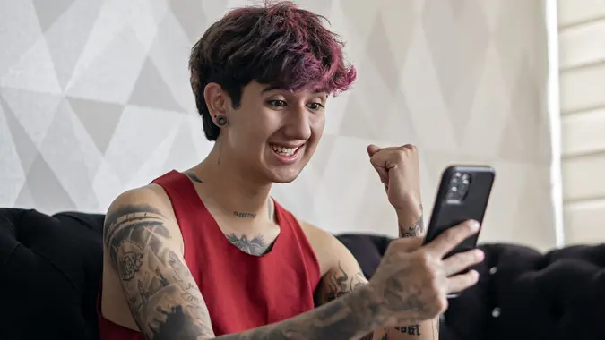 Excited young adult looking at phone with fist in the air.