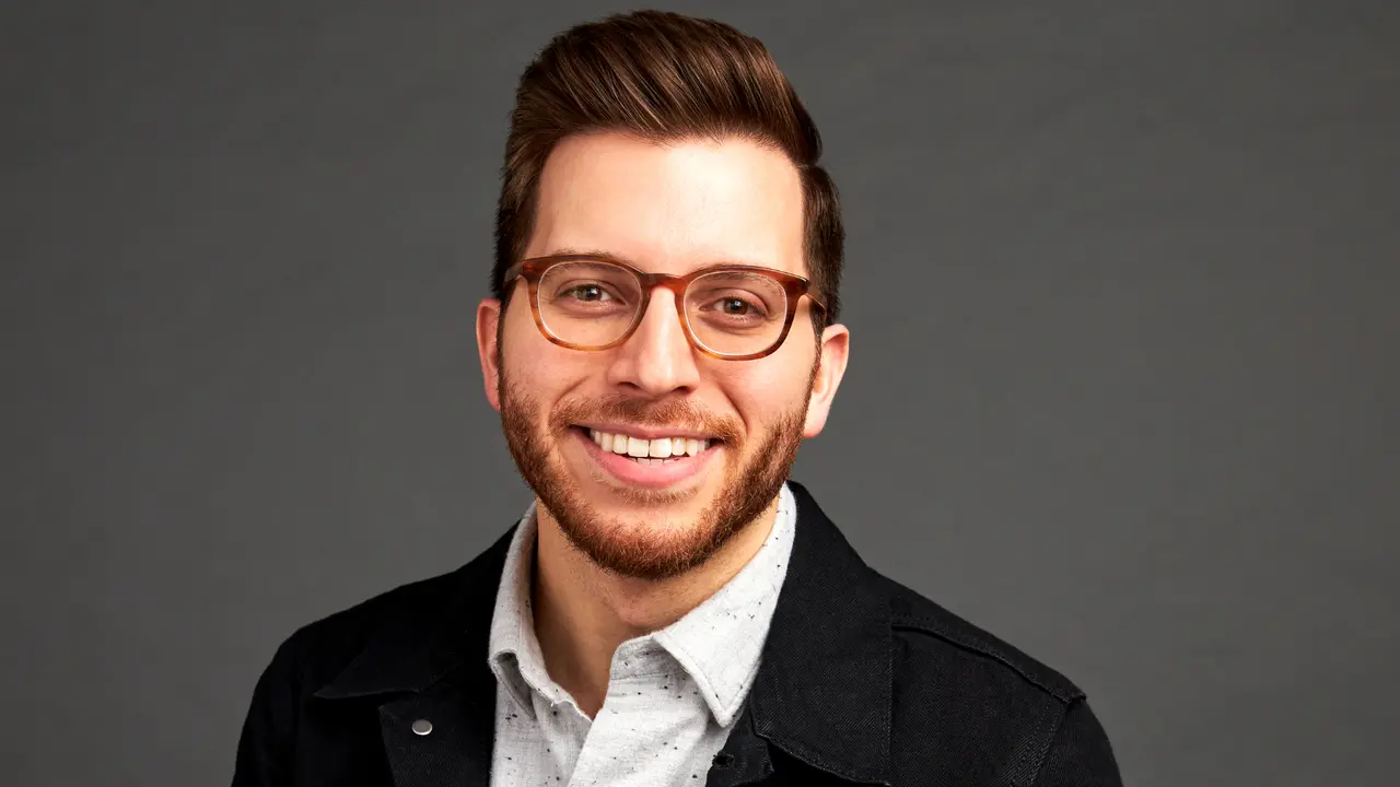 George Kamel smiling at the camera with a grey background