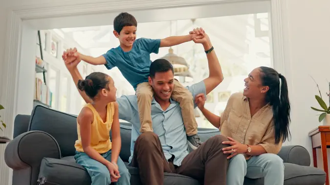 Smiling family of four sits on a couch laughing and enjoying time together at home.