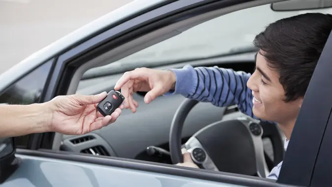 A teen driver smiling as they receive car keys, capturing the excitement of getting their first car.