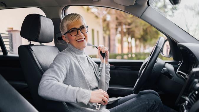 Portrait of happy senior woman fastening seat belt before driving a car.