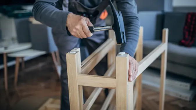 One senior carpenter in work suit putting together wooden table and using hummer.