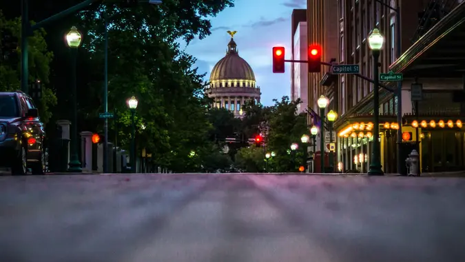 Shot of Jackson Mississippi State Capitol Building set against a sunrise and flanked with trees and streetlights