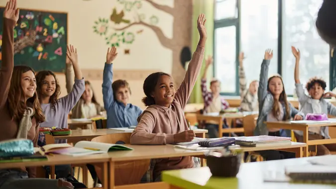 Happy elementary school students raising hands in classroom, engaged in learning and participating in a lesson.