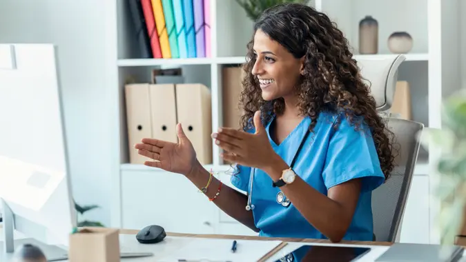 Shot of female nurse explaining medical treatment to patient through a video call with computer in the consultation.