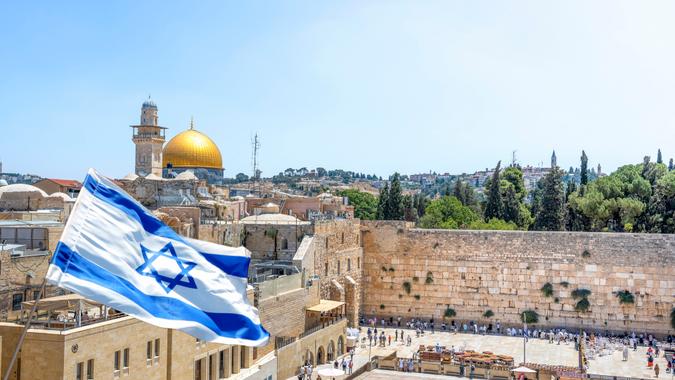 Jerusalem, Israel - September 5, 2022; An Israeli flag blows in the wind from an elevated view of the Western Wall and the Al-Aqsa Mosque in Jerusalem.