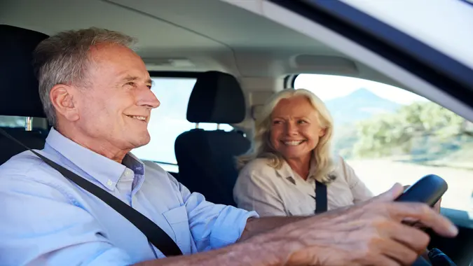 Senior white man driving car, his wife beside him in the front passenger seat, close up, side view.