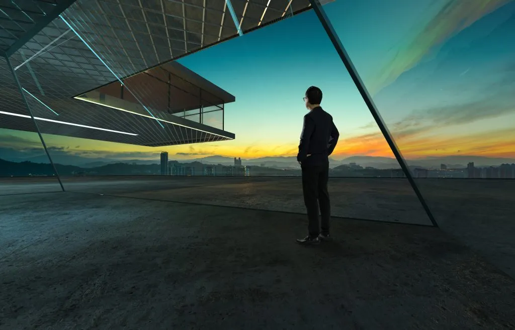 Businessman looks at sunrise thoughtfully with steel and glass facade modern building background .