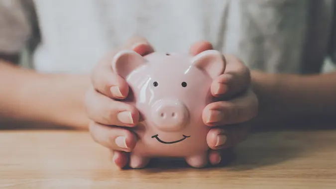 Panoramic image, Man hand holding piggy bank on wood table. Save money and financial investment stock photo