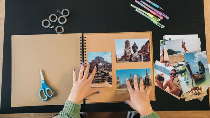 Image seen from above of a middle-aged woman's hands placing the photos and markers to make her handmade travel kraft paper photo album. stock photo