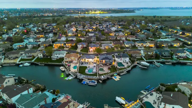 Small illuminated town on sea channel bank with boats and yachts on piers against cloudy sky, twilight in Nassau County, New York.