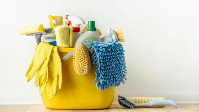 Brushes, bottles with cleaning liquids, sponges, rag and yellow rubber gloves on white background.