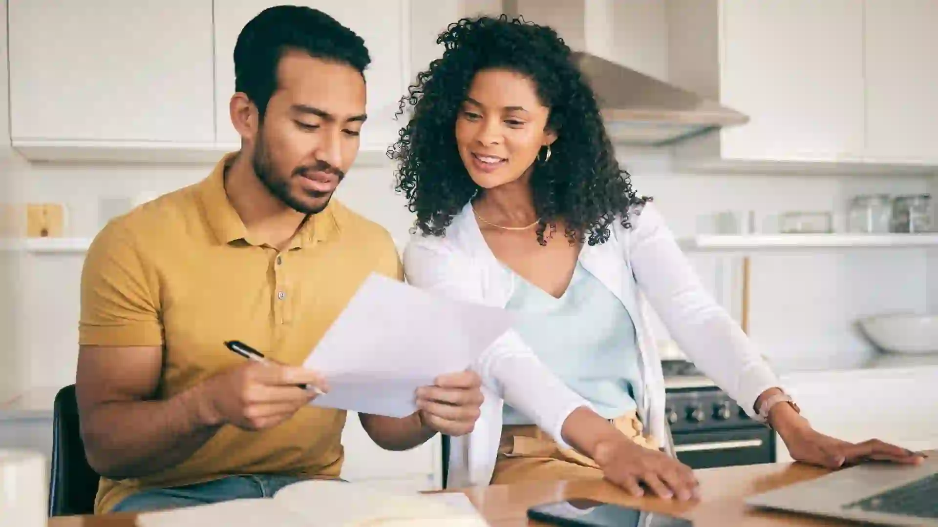 A young couple sitting at their kitchen table, reviewing financial documents and managing their household bills.