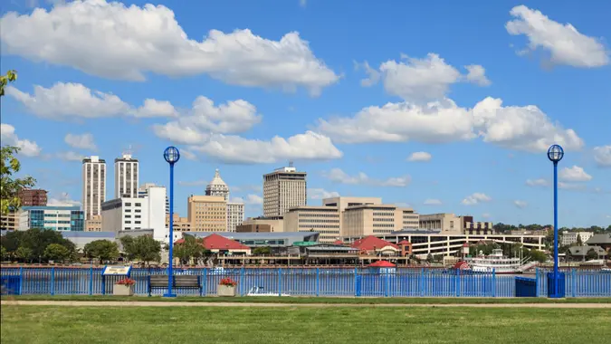 View of Peoria's river front showing downtown Peoria buildings, bridge, the Illinois river, historic paddle boat with blue blue sky and clouds in background.