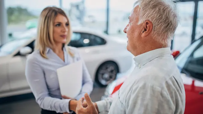 Beautiful saleswoman shaking hand with senior man at the car showroom