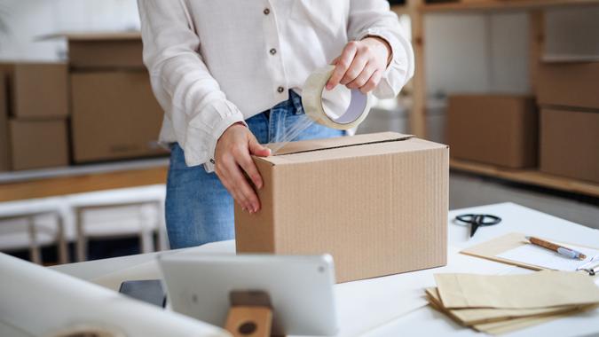 Midsection of unrecognizable woman dropshipper working at home, packing parcels.