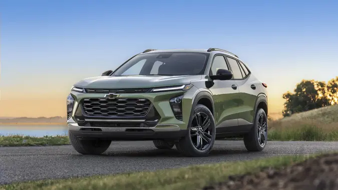 Front 3/4 view of 2025 Chevrolet Trax ACTIV in Cacti Green parked on a road in front of a lake.