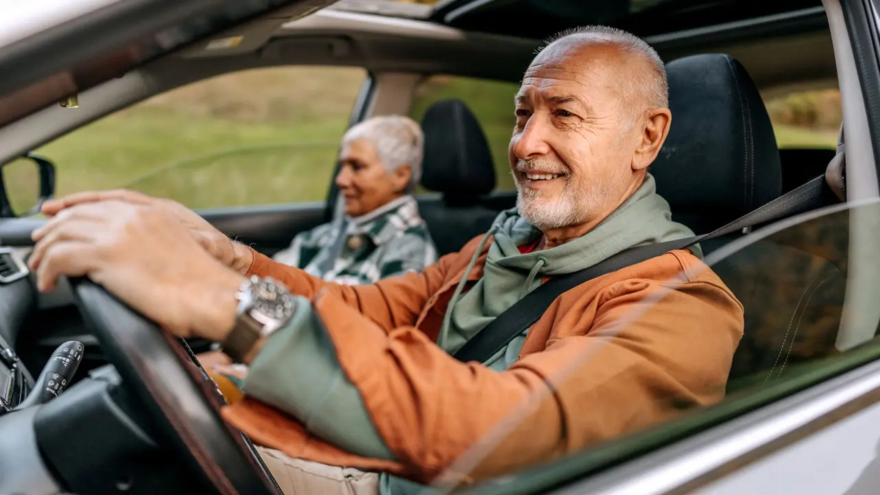 Smiling retired couple sits in a car on a sunny road trip, enjoying their journey together.