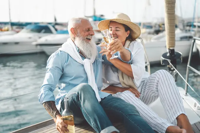 Senior couple toasting champagne on sailboat vacation - Happy seniors having fun celebrating their wedding anniversary on a boat trip - Romance relationship and travel lifestyle concept.