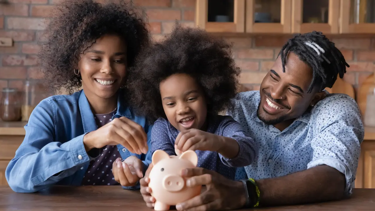 Caring young African American parents teaching small daughter saving money, stock photo