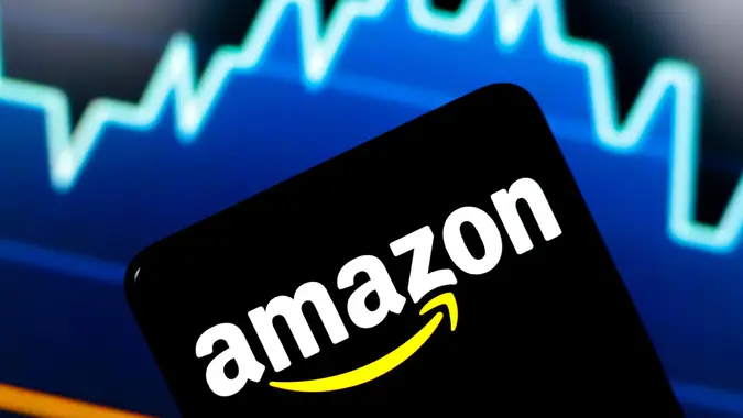 The Amazon logo displayed on a smartphone with a stock chart in the background.