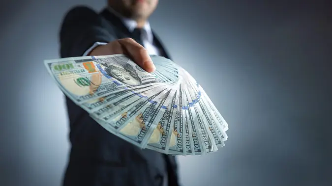 A man wearing a suit is holding a wad of cash and showing it off.