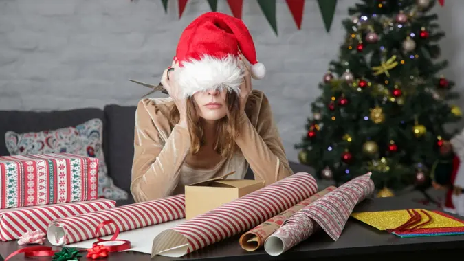 Depressed frustrated woman wrapping Christmas gift boxes, winter holiday stress concept.