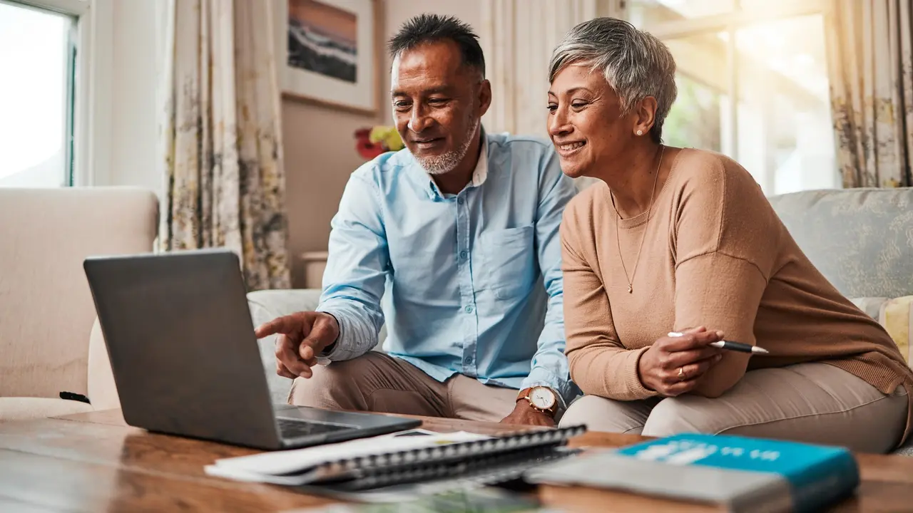 Picture of a mature couple on sofa using a laptop for planning finances, retirement, budget and more.