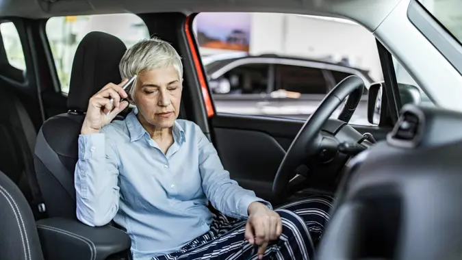 Mature woman sitting in a car at showroom while feeling pain in her head.