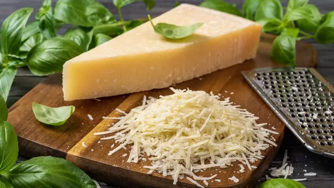 Shredded parmesan cheese and grater on a cutting board.