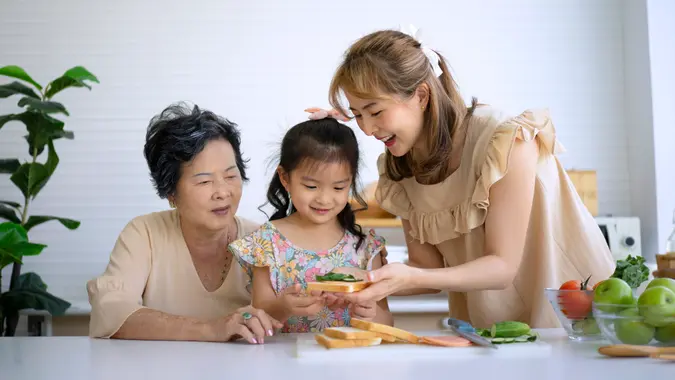 Grandmother, mother and granddaughter prepare food in the kitchen.