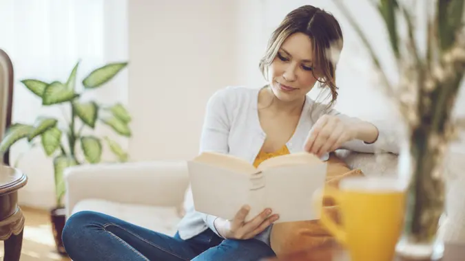 Content woman is reading a book on a white sofa at home.