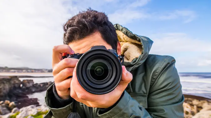A young man using a DSLR camera at the sea.