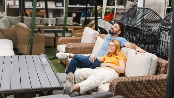 Portrait of smiling loving young couple sitting on the sofa garden terrace in the furniture department of store.